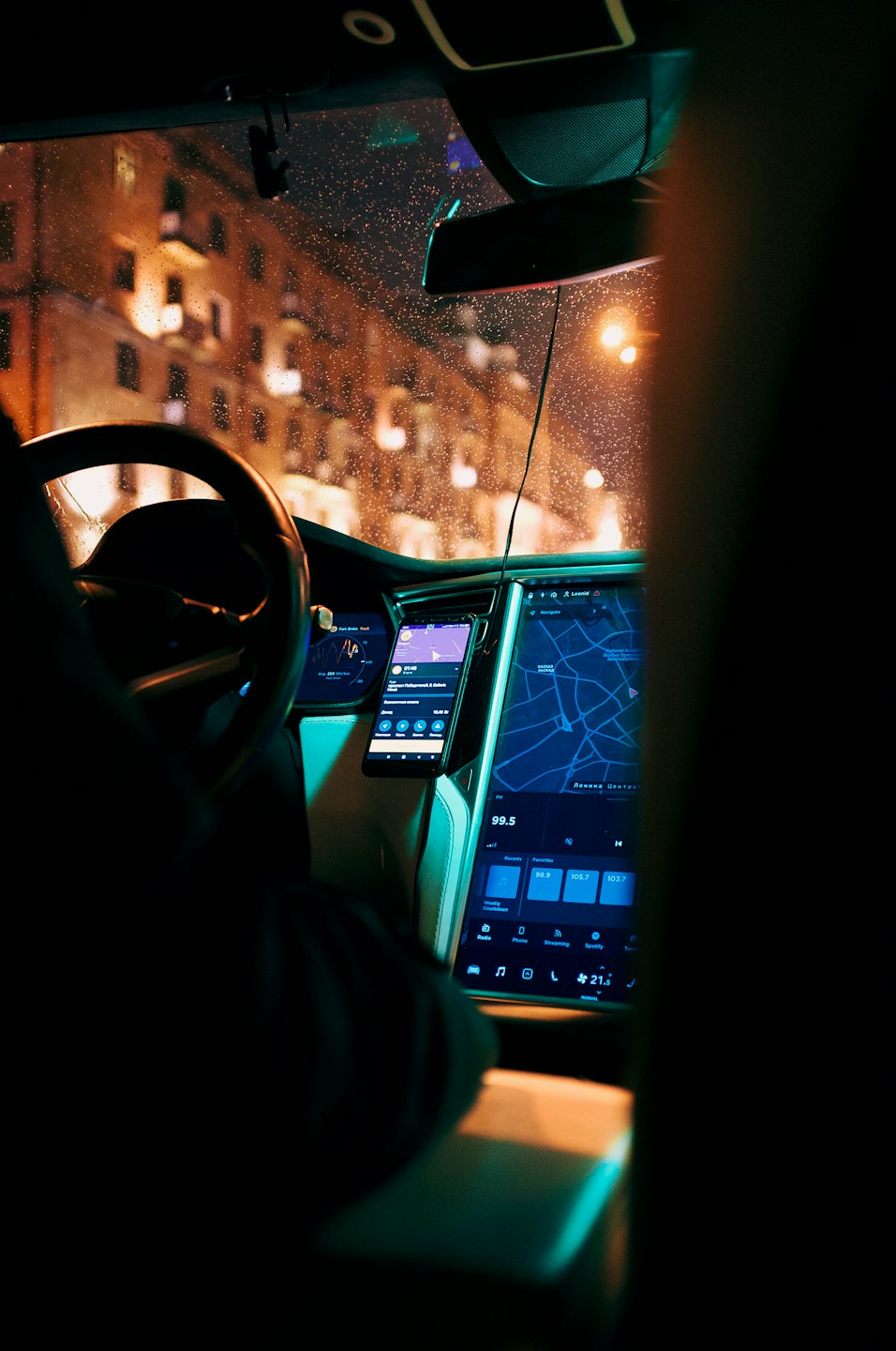 Driver's view of a car's dashboard with smartphone and touchscreen map at night.