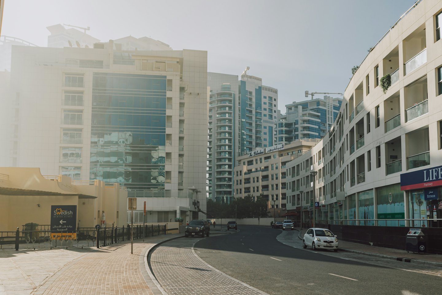 A modern city street with cars on a road and multi-story buildings.