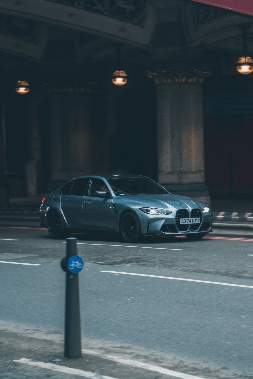 A grey sports sedan drives past a classical building at dusk.