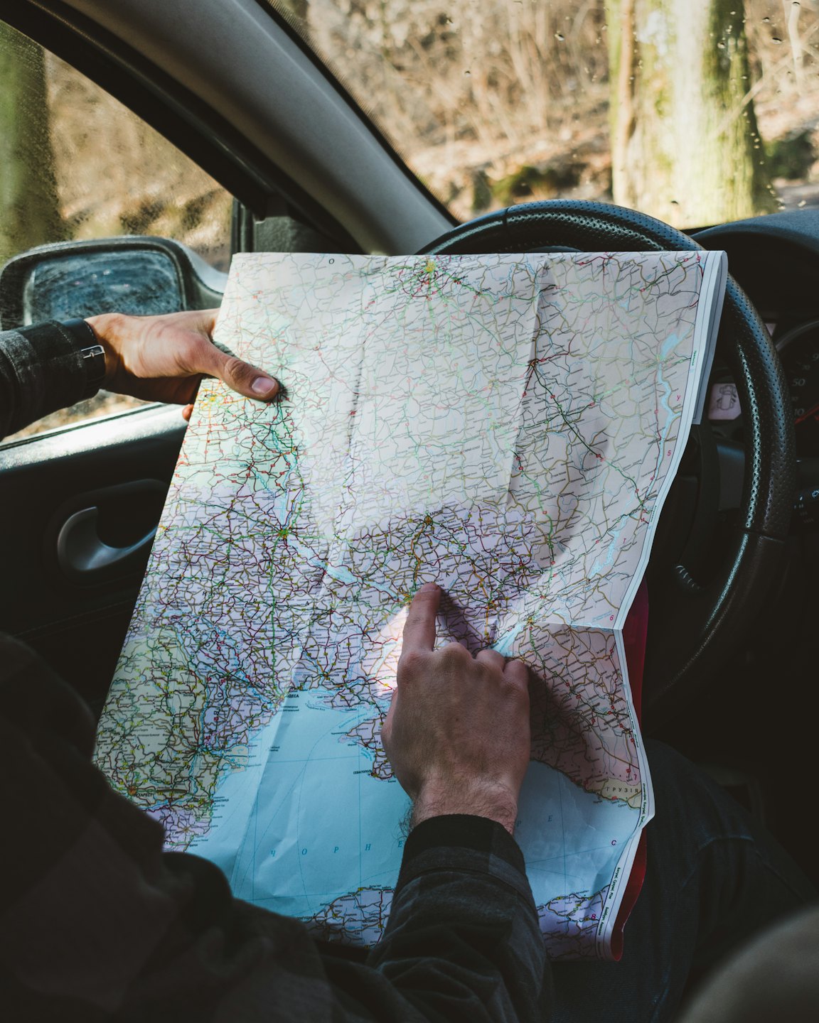 Driver pointing at a paper map inside a car.